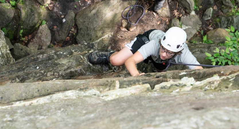 From above, you can see a rock climber wearing safety gear making their way up a rock wall